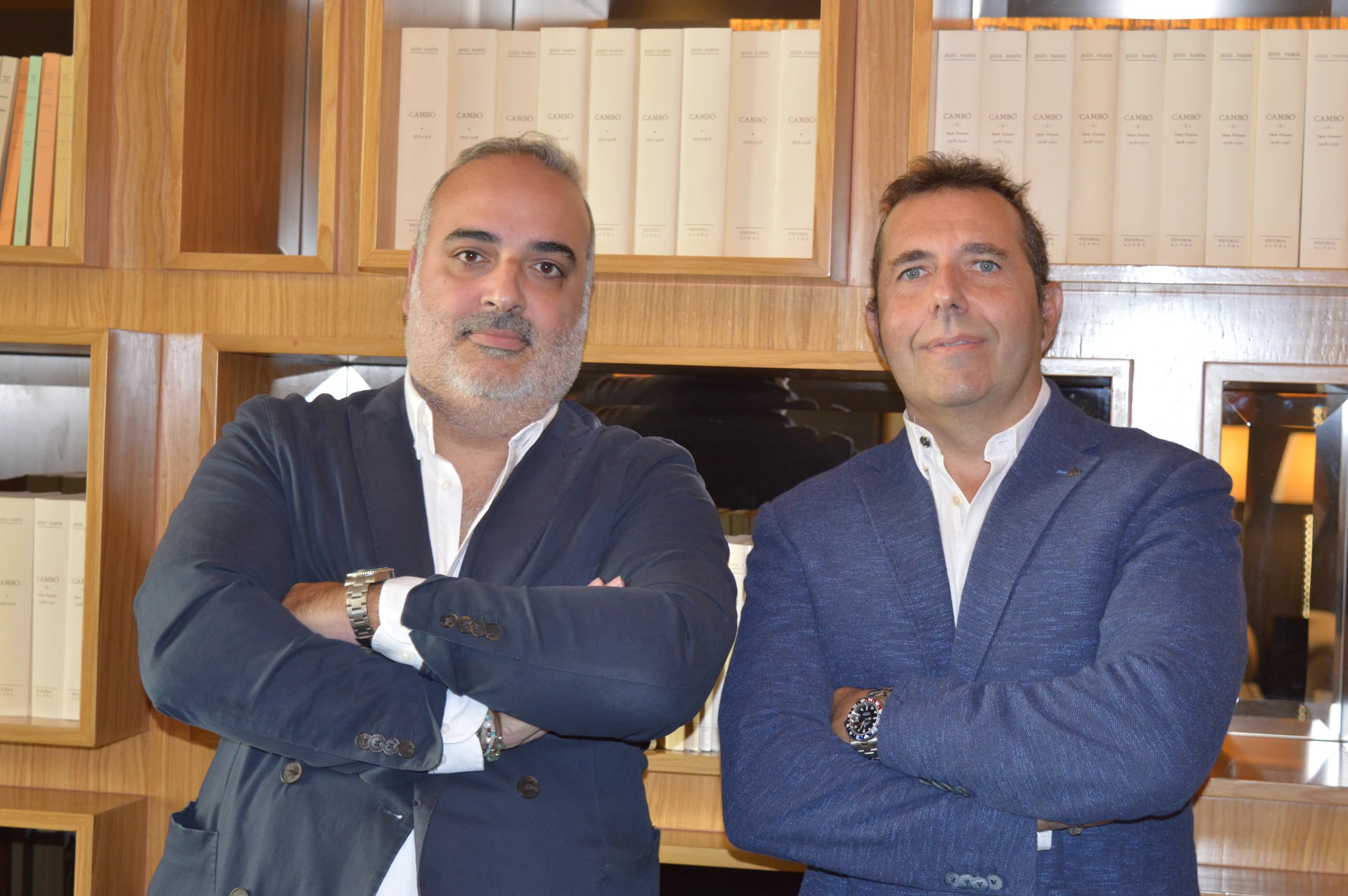 Juan Luis y Rubén, socios de Clapham+Partners, con los brazos cruzados frente a una librería de madera