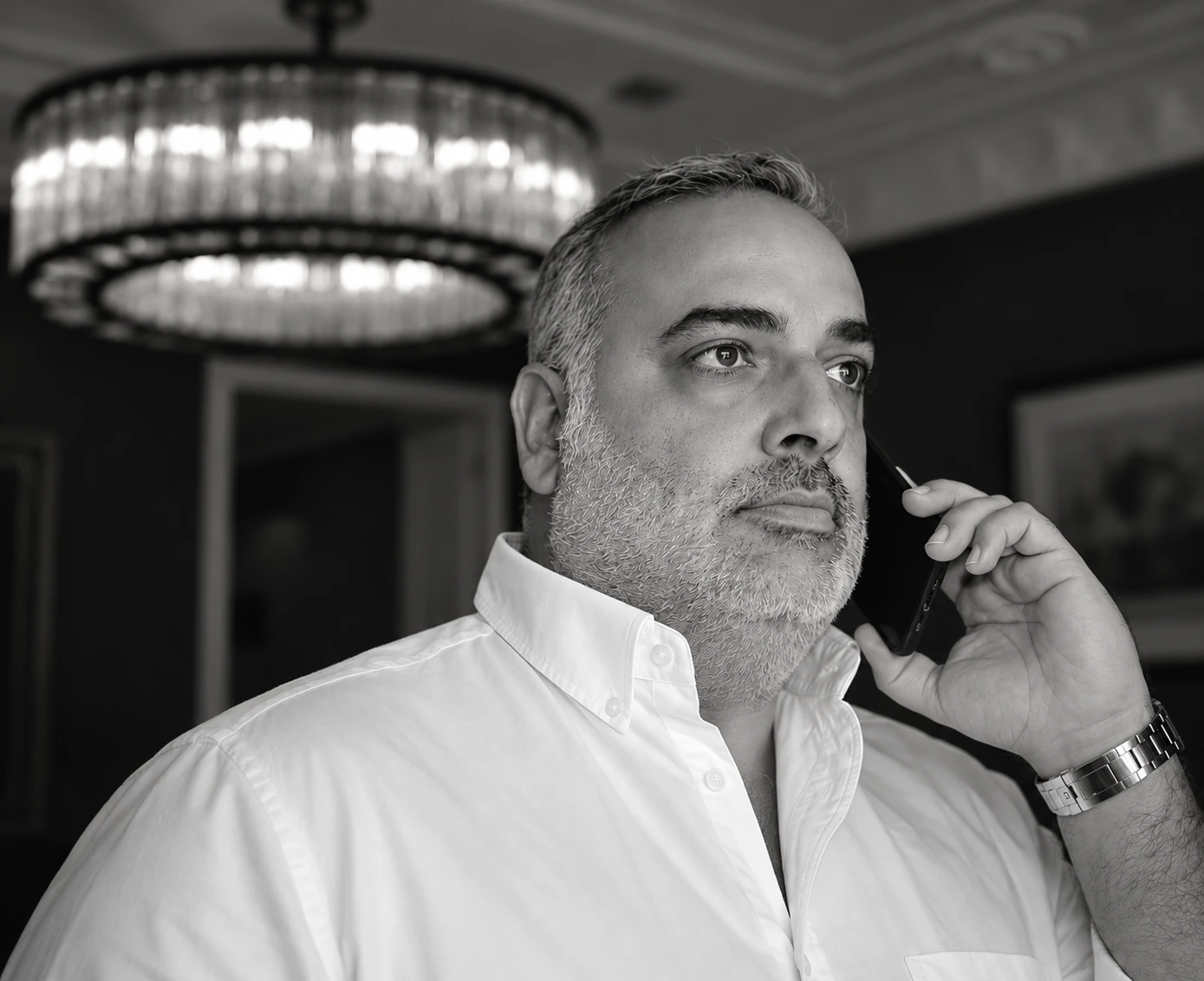 Juan Luis, socio de Clapham+Partners, con camisa blanca y hablando por teléfono bajo una lámpara de cristal, en blanco y negro