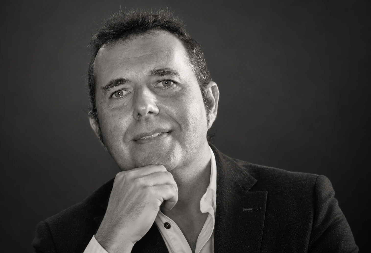 Rubén, socio de Clapham+Partners, con americana oscura, camisa blanca y la mano bajo la barbilla, en un retrato de estudio en blanco y negro